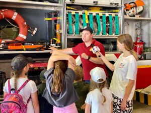 Преподаватель учебно-методического центра демонстрирует детям инструменты и технику пожарных